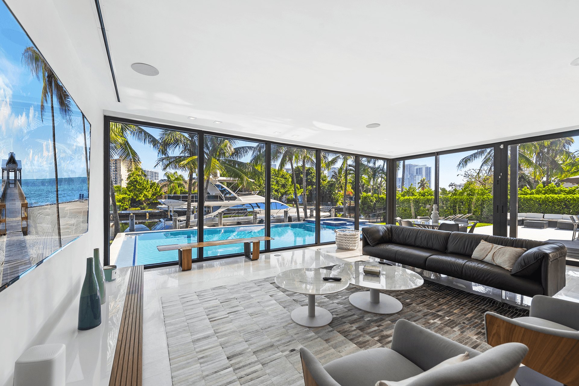 Luxurious living room at Villa Okasa featuring modern decor, a private indoor swimming pool, and a scenic view of a yacht docked outside.