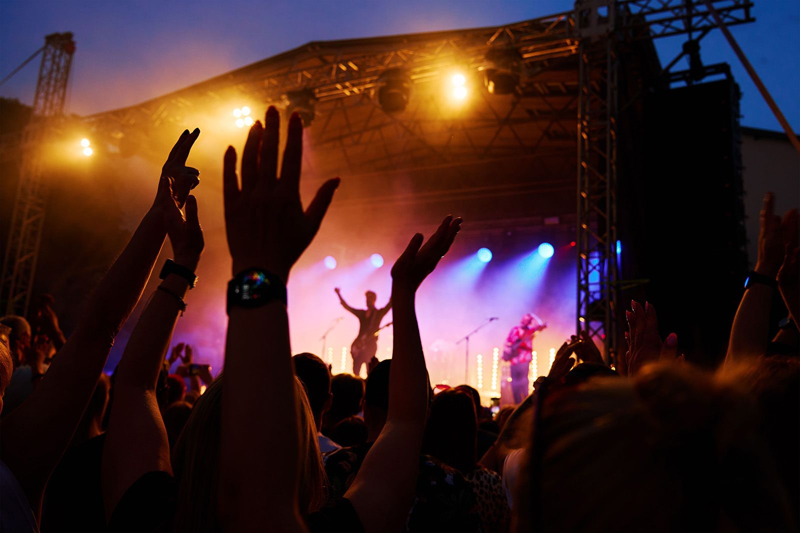 Excited crowd at a live music festival in Miami, with hands raised as the band performs on a vibrant, illuminated stage, capturing the energy of the concert.