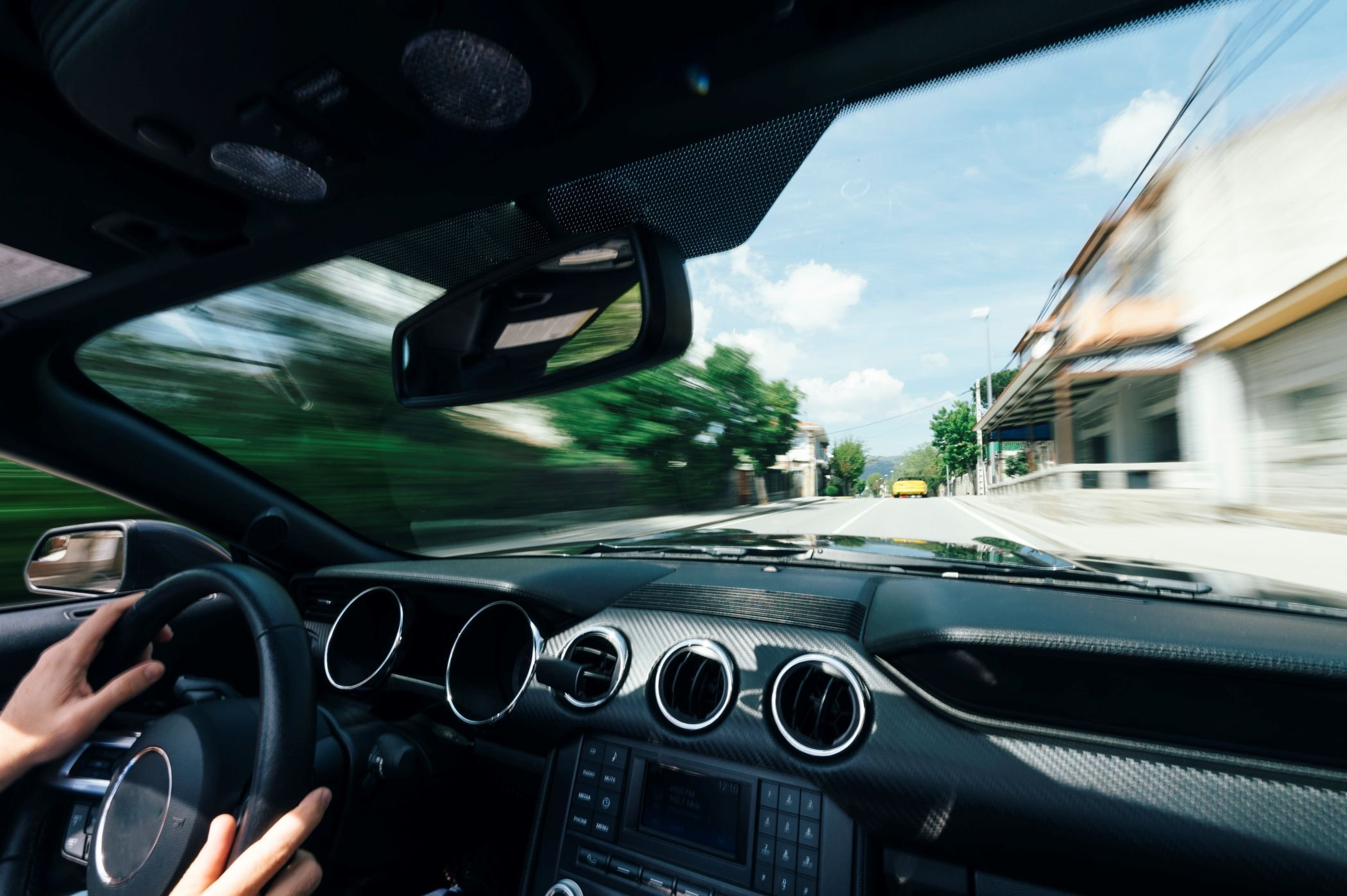 Driving a luxury car rental through the streets of Miami, experiencing a smooth and exhilarating ride with high-end performance and comfort. Showing hands on a steering wheel and a high-end interior as well as blurred outside beyond the windshield.