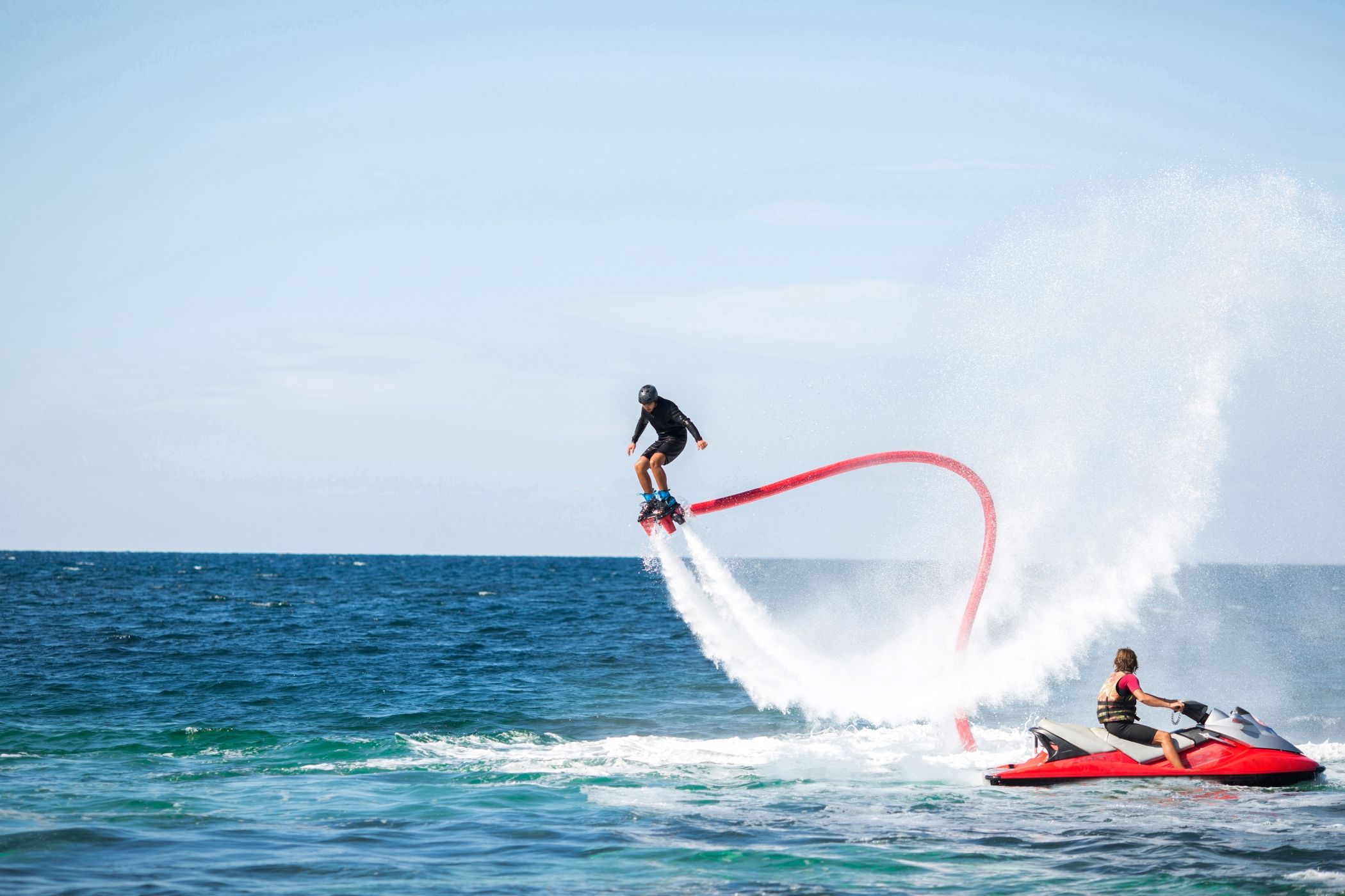 Person flyboarding high above the ocean, propelled by water jets, with a jet ski nearby, capturing the thrill and excitement of this high-adrenaline water sport near Miami.