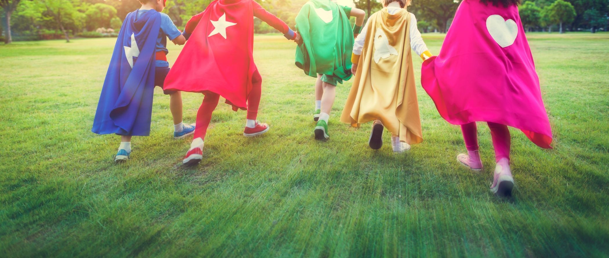 Group of children dressed in superhero capes running across a grassy field, capturing the fun and excitement of a cosplay event like Florida SuperCon in Miami.