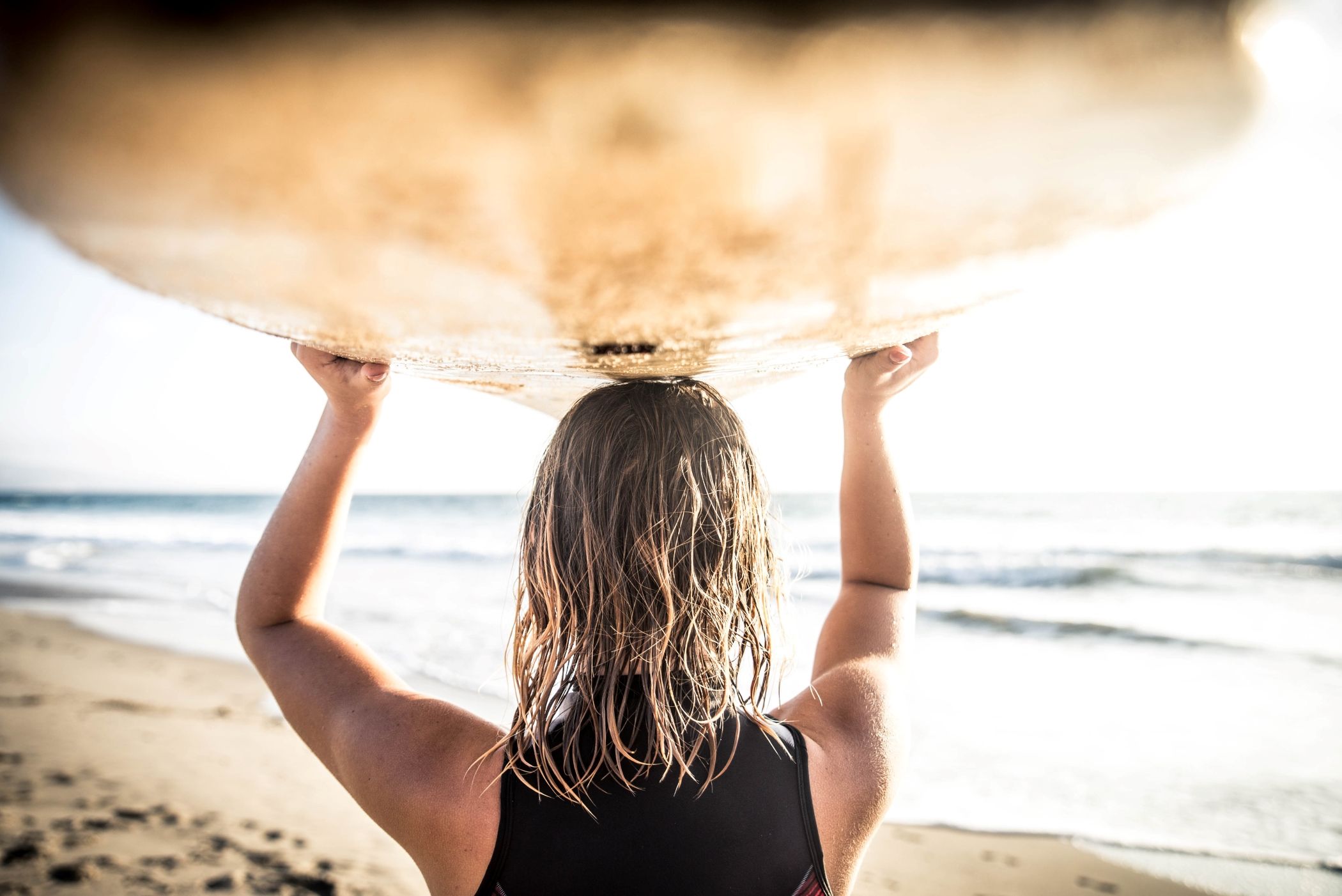 Woman carrying surf board over her head on a beach in Miami.