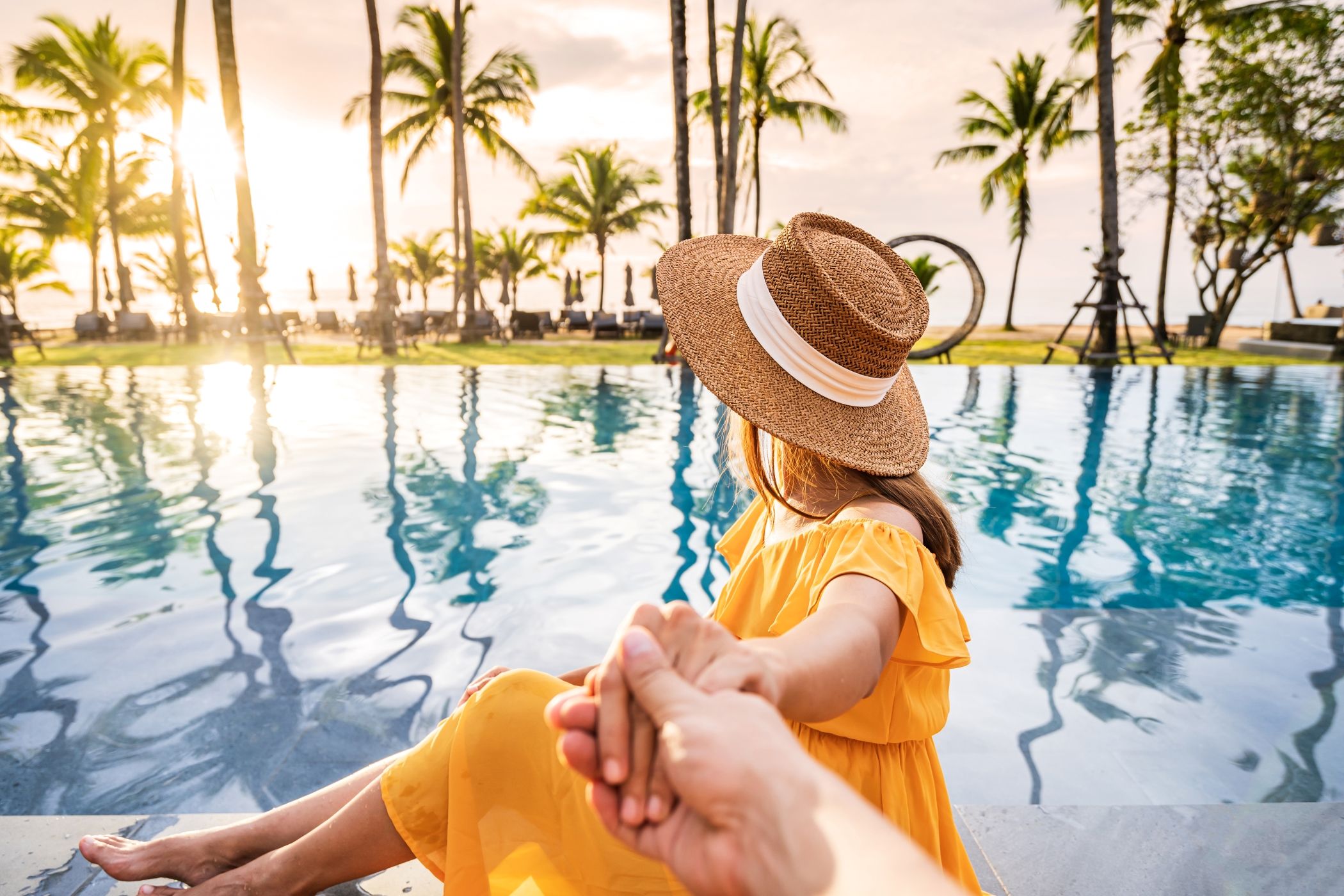 Young woman relaxing and enjoying the sunset by a tropical resort pool in Miami and another person off camera is holding her hand lovingly.